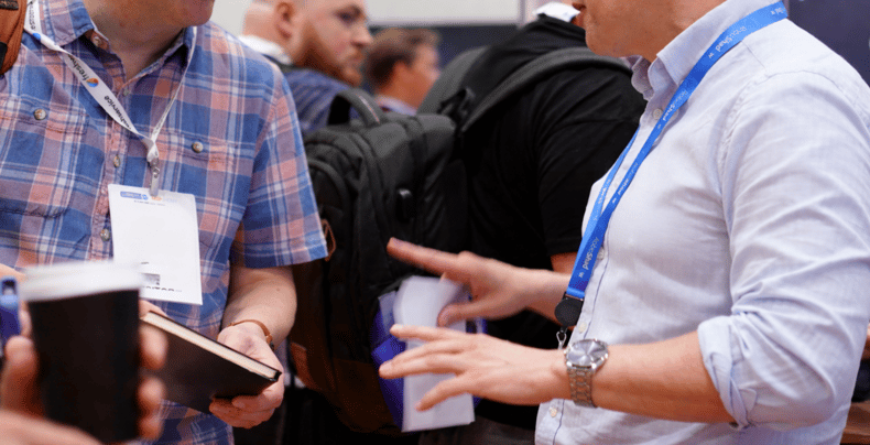 Two people talk at a busy MSP networking event, with one holding a notebook while the other gestures during the conversation.